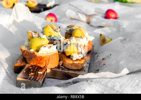 Food on outdoor summer or spring picnic in forest on sunny meadow, bruschetta with cheese and pear, snacks, apples, wooden plate. Concept romantic lun Stock Photo