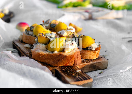 Food on outdoor summer or spring picnic in forest on sunny meadow, bruschetta with cheese and pear, snacks, apples, wooden plate. Concept romantic lun Stock Photo