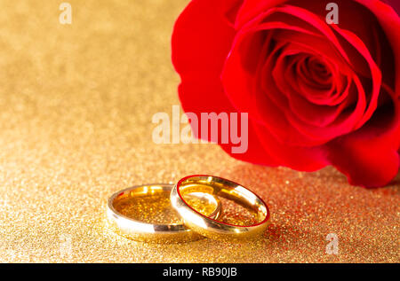 Gold Wedding Bands and a Red Rose on a Golden Glitter Background Stock Photo