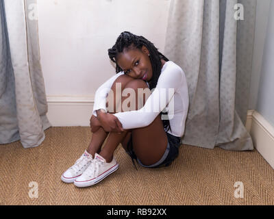 Pretty young woman in denim shorts and white top sitting on the floor Stock Photo