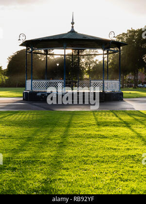 The Victorian bandstand in the Royal Pump Room gardens, Leamington Spa, England UK, with low sun behind casting long shadows.