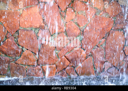 Artificial waterfall in the amusement Park. Flowing water on the background of natural red stone Stock Photo