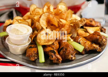 Bar Food:  Chicken wing platter from side with curly potatoe chips and celery.  White sauce served with platter. Stock Photo