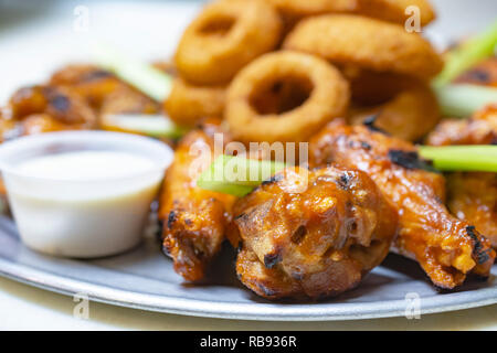 Bar Food:  Chicken wing platter up extreme close.  White dipping sauce on the side.  Onion rings blurred in the background. Stock Photo