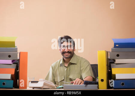 Smiling businessman looking at files sitting at his office desk with a glass of tea in his hand. Stock Photo