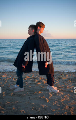 two teenage boys wearing similar clothes fool about on a beach by leaning against each other as the sunsets in southern france Stock Photo