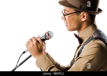 side view of happy mixed race young man in hat singing in microphone isolated on white Stock Photo