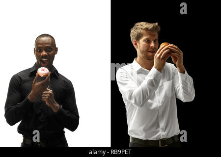 Men eating a hamburger and donut on a black and white background. The happy afro and caucasian men. The burger, fast, unhealthy food concept Stock Photo
