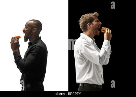 Men eating a hamburger and donut on a black and white background. The happy afro and caucasian men. The burger, fast, unhealthy food concept Stock Photo