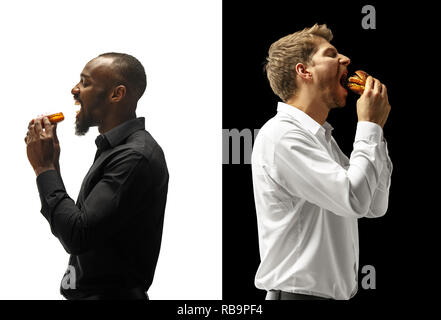 Men eating a hamburger and donut on a black and white background. The happy afro and caucasian men. The burger, fast, unhealthy food concept Stock Photo