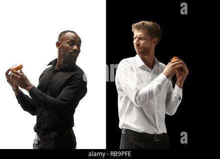 Men eating a hamburger and donut on a black and white background. The happy afro and caucasian men. The burger, fast, unhealthy food concept Stock Photo