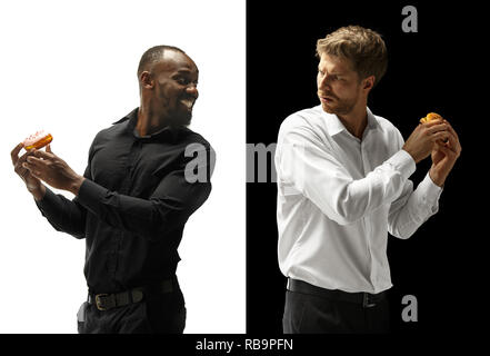 Men eating a hamburger and donut on a black and white background. The happy afro and caucasian men. The burger, fast, unhealthy food concept Stock Photo