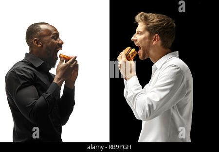 Men eating a hamburger and donut on a black and white background. The happy afro and caucasian men. The burger, fast, unhealthy food concept Stock Photo