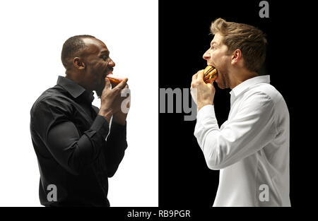 Men eating a hamburger and donut on a black and white background. The happy afro and caucasian men. The burger, fast, unhealthy food concept Stock Photo