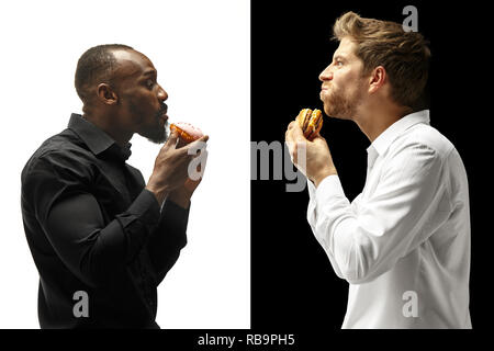Men eating a hamburger and donut on a black and white background. The happy afro and caucasian men. The burger, fast, unhealthy food concept Stock Photo