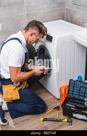adult repairman working with screwdriver while repairing washing machine in bathroom Stock Photo