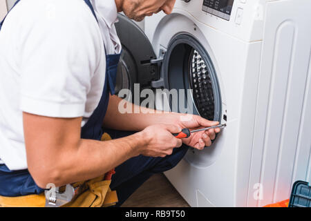 cropped view of adult repairman working with screwdriver while repairing washing machine in bathroom Stock Photo