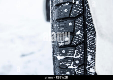 Closeup view of car tire with metal studs pikes outdoors on snowy icy road outdoors in winter. Helps stop and control car better on icy roads concept. Stock Photo