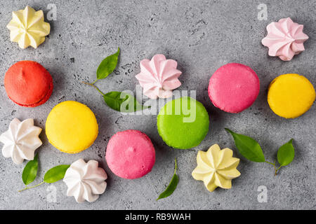 Colorful various French sweet macaroons dessert cake macarons and pastel Meringue Marshmallow on gray background decorated with green leaves top view  Stock Photo