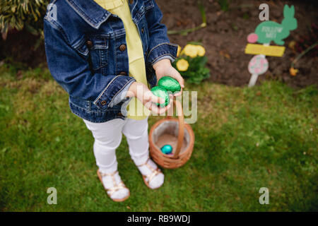 HIgh angle view of an unrecognsiable child. They are holding their hands together, cupped, with chocolate easter eggs inside. She has a basket at her  Stock Photo