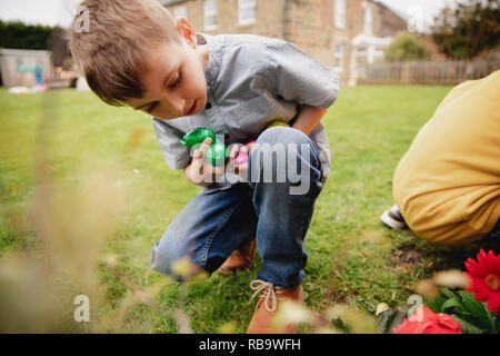 Young boy on an easter egg hunt with a friend. They are seaching for chocolate easter eggs in a back garden. Stock Photo