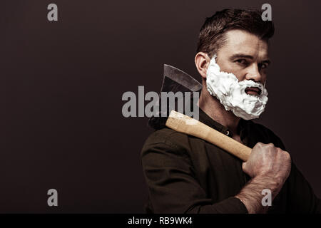 handsome bearded man in brown shirt holding axe and looking at camera isolated on brown Stock Photo
