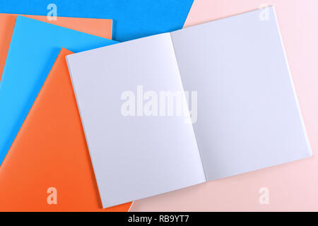 Open notebook and colorful notebooks on blue and pink background. Stock Photo