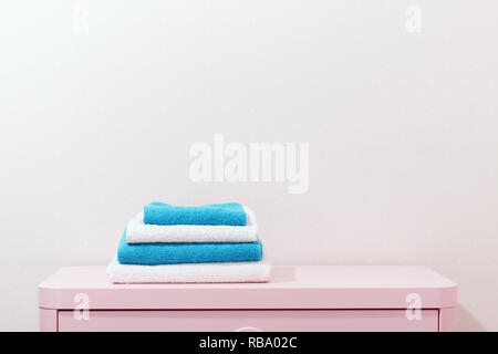 On a pink dresser there is a stack of white and blue towels. Stock Photo