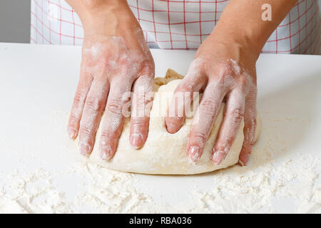 Woman kneads raw fresh dough with hands on the table Stock Photo