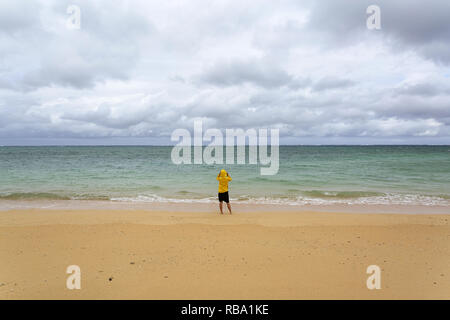 Young woman in yellow jacket standing, walking in shallow water on a beautiful secluded beach, Ishigaki, Japan Stock Photo