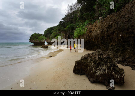 Mother and son walking on dramatic sandy beach with limestone scultures at Ibaruma Sabichi Cave, Ishigaki, Japan