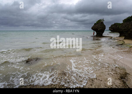 Young boy standing under limestone sculpture by the sea at sandy beach at Ibaruma Sabichi Cave, Ishigaki, Japan