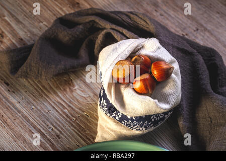 Horizontal photo with several nuts. Hazelnuts are placed in white linen bag with blue ornament. Bag is placed on wooden board with white and brown vin Stock Photo
