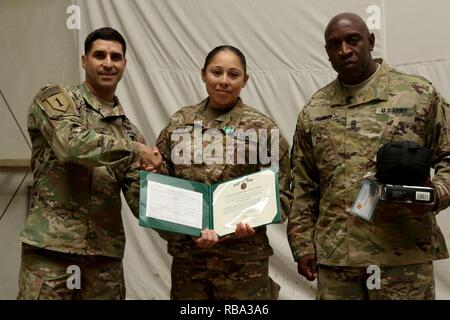 U.S. Army Staff Sgt. Miriam Reyes, a squad leader in Headquarters and Headquarters Company, 1st Battalion, 67th Armor Regiment, 3rd Armored Brigade Combat Team, 1st Armored Division, receives her award from the 1st Battalion, 77th Armor Regiment command team, Lt. Col. Johhny Casiano and Command Sgt. Maj. Maurice Peebles, after winning the Top Medic Competition at Camp Buehring, Kuwait, Dec. 19, 2016.  The stressful 36-hour competition, hosted by 3rd Armored Brigade Combat Team, 1st Armored Division, tested the Soldiers’ basic warrior skills, medical skills proficiency, and overall physical str Stock Photo