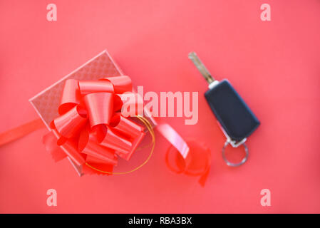 Give gift car key concept / Red gift box with red ribbon bow and key car as present on red background Stock Photo