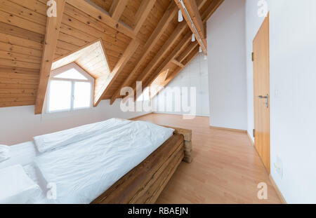bright light modern simple master bedroom with wooden parquet floors and designer closet and traditional wooden beam bed under slanted ceiling in a re Stock Photo