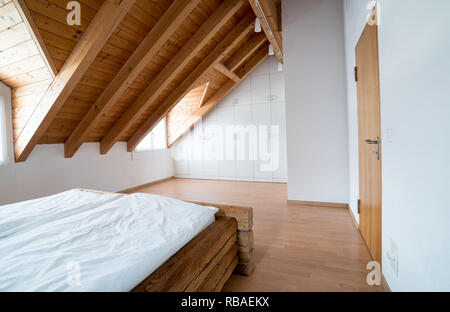 bright light modern simple master bedroom with wooden parquet floors and designer closet and traditional wooden beam bed under slanted ceiling in a re Stock Photo