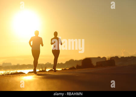Silhouette of a couple practicing sport running at sunset on the road Stock Photo
