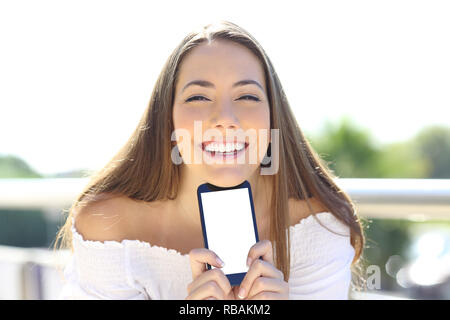 Front view portrait of a happy woman smiling showing a blank smartphone screen outdoors Stock Photo
