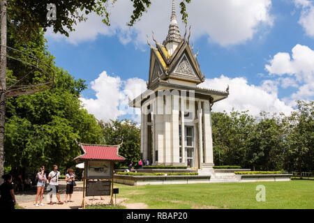 The Killing Fields Genocidal Centre memorial site with Buddhist Stupa containing human skulls and tourists reading sign Choeung Ek Phnom Penh Cambodia Stock Photo