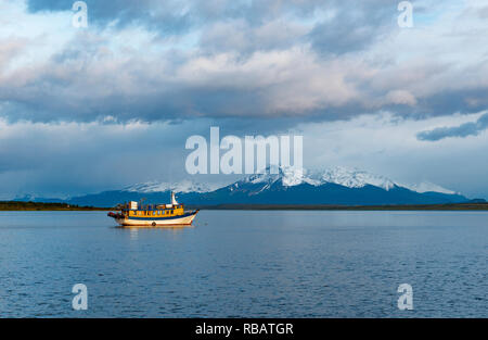 Landscape of the Last Hope Sound at sunrise with a fishing boat and snowcapped Andes peaks in the background, Puerto Natales, Patagonia, Chile. Stock Photo