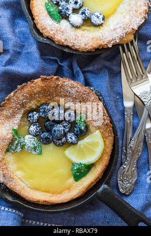 Fresh homemade Dutch Baby pancake with lemon curd and blueberries in iron skillets. Top view. Stock Photo