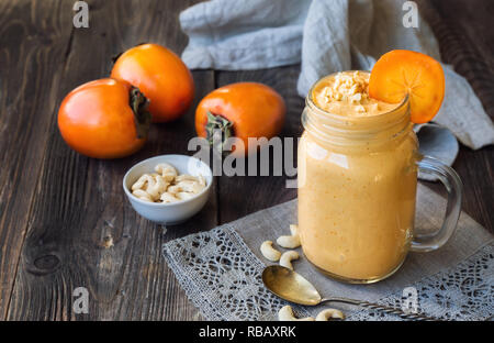 Smoothie with persimmon and cashew nuts injar on rustic wooden background. Stock Photo