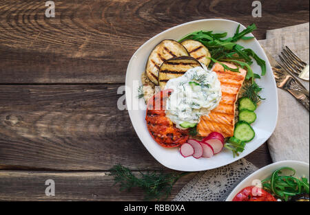 Grilled salmon, eggplants and tomatoes with quinoa and tzatziki sauce on rustic wooden background. Healthy dinner. Top view. Stock Photo