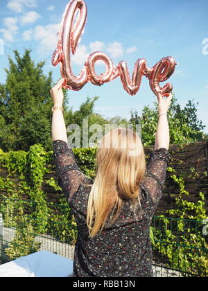 Girl holds a ballon in the air that says love, outside with the blue sky in the background. Stock Photo