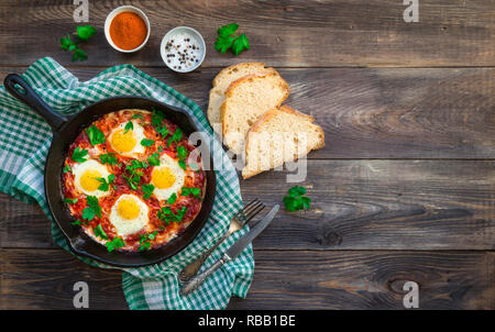 Fried eggs with vegetables and tomato sauce in iron skillet on rustic wooden background. Traditional Israeli dish Shakshuka. Healthy breakfast. Top vi Stock Photo