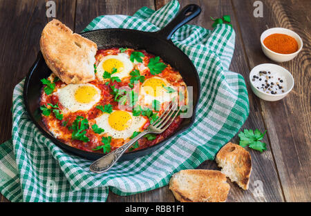 Fried eggs with vegetables and tomato sauce in iron skillet on rustic wooden background. Traditional Israeli dish Shakshuka. Healthy breakfast. Stock Photo