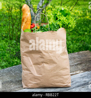 A full paper bag of healthy products stands on the wooden table, side view. Stock Photo