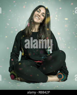 Pretty girl sitting under a colored confetti rain. Stock Photo