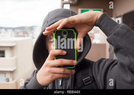 Boy holding smartphone taking photo wearing hoodie Stock Photo